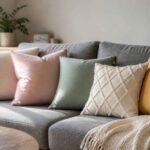 Szara sofa z pastelowymi poduszkami, kocem i rośliną w jasnym salonie